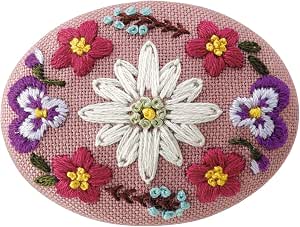 Oval embroidered brooch showing a white central flower surrounded by red and purple flowers on pink fabric.