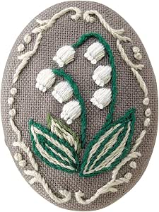 Oval embroidered brooch with white flowers, green stems and leaves, and a decorative border on gray fabric.