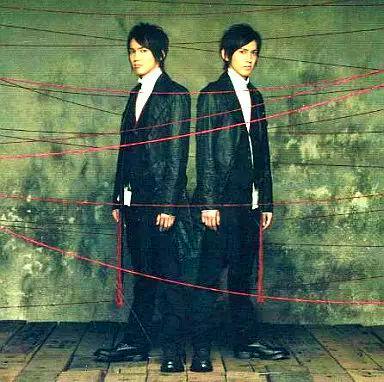 CD/DVD cover art showing two men in dark suits standing back-to-back against a concrete wall with red string.