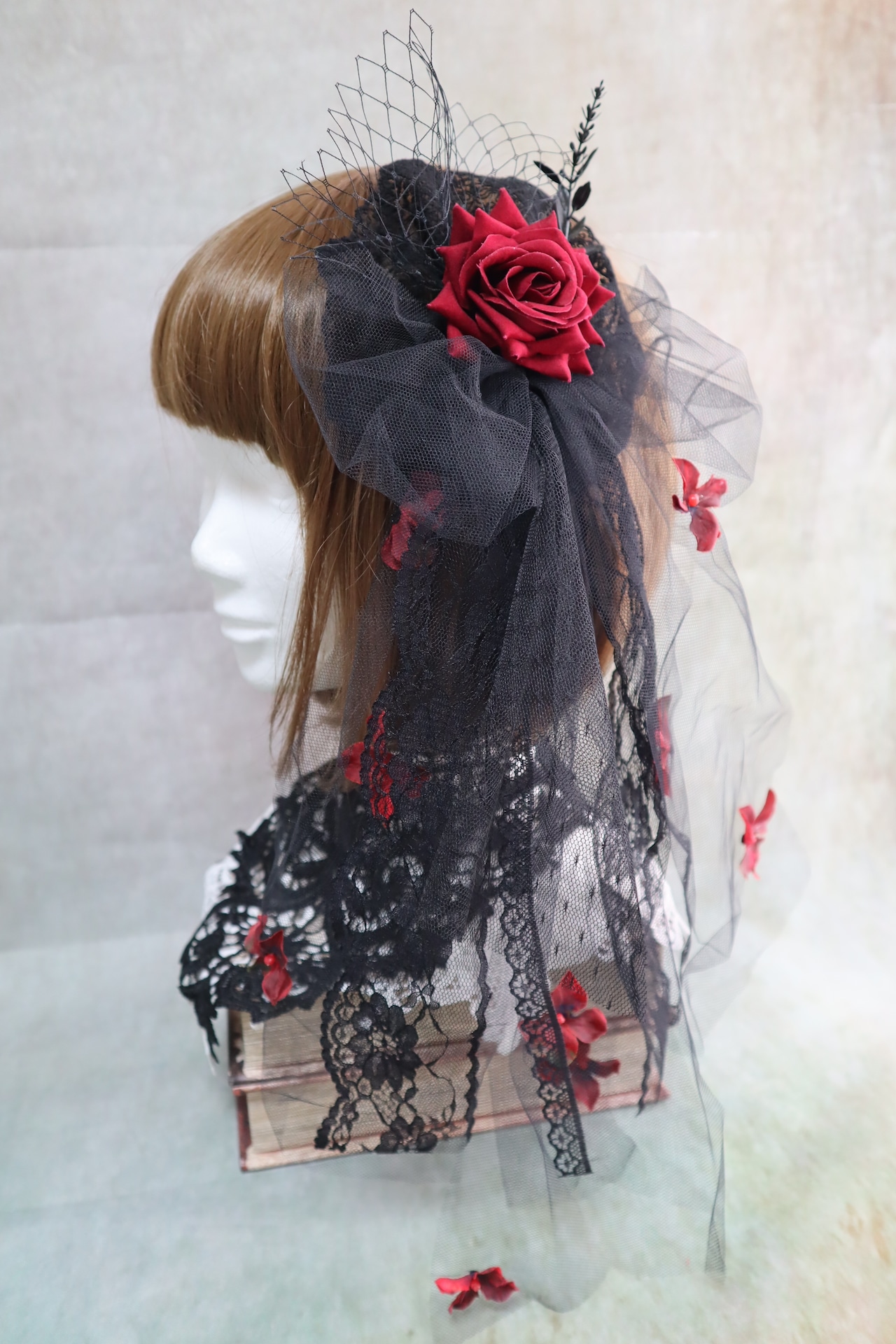 Black tulle headpiece with a wine-red rose and lace accents displayed on a mannequin head.