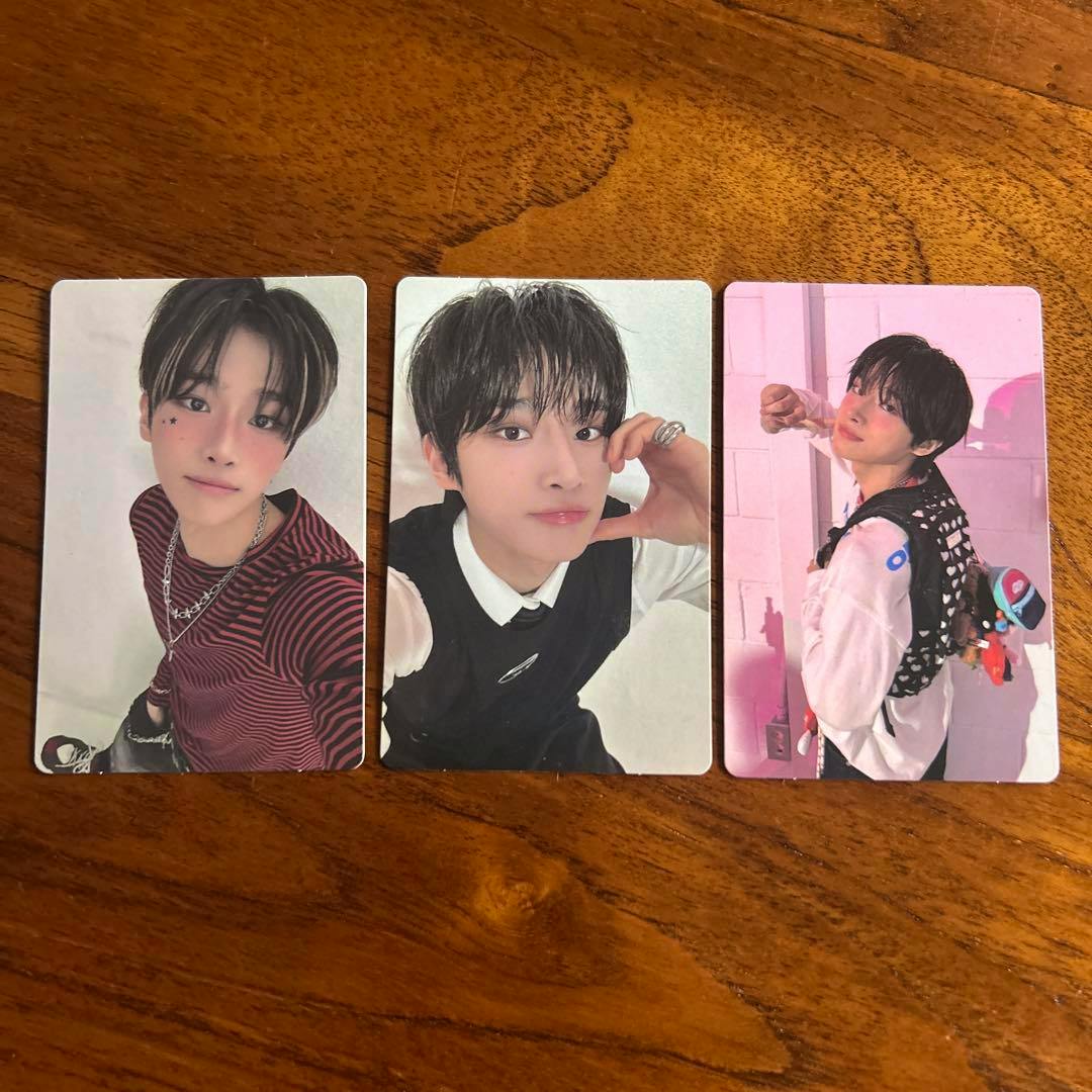 Three photocard fronts showing portrait photos of the artist laid side-by-side on a wooden surface.