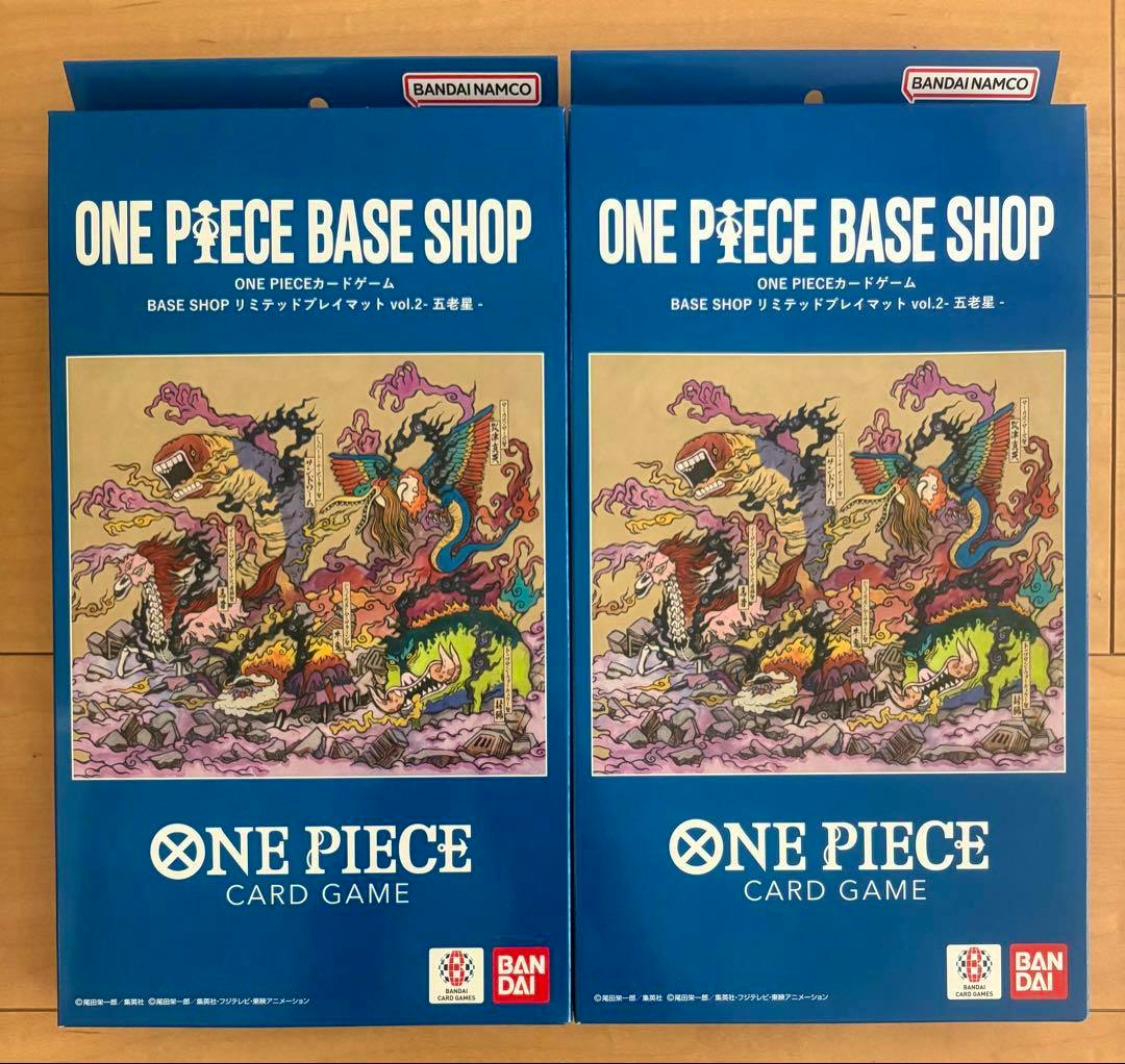 Two boxed ONE PIECE BASE SHOP limited playmat vol.2 packages with blue packaging and illustrated artwork shown on a wooden surface.