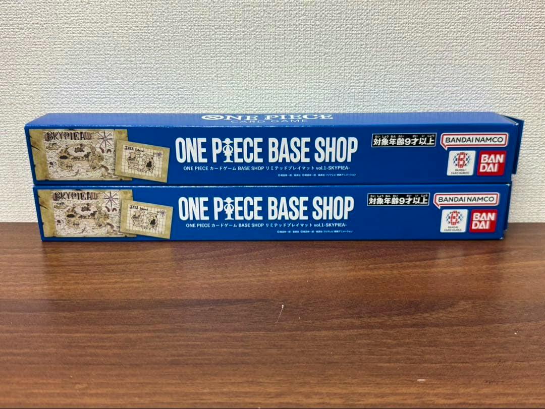 Two boxed ONE PIECE BASE SHOP playmats in blue packaging stacked on a wooden surface.