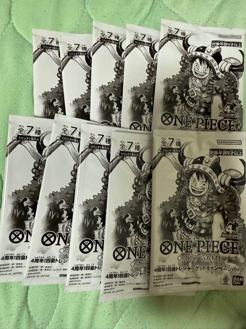 Ten sealed One Piece Card Game 4th Anniversary campaign packs laid out on a green quilted surface.