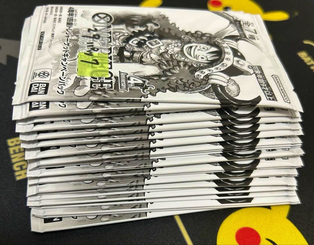 A stack of sealed ワンピースカードゲーム 4周年四皇トレジャーゲットキャンペーンパック booster packs stacked on a playmat.