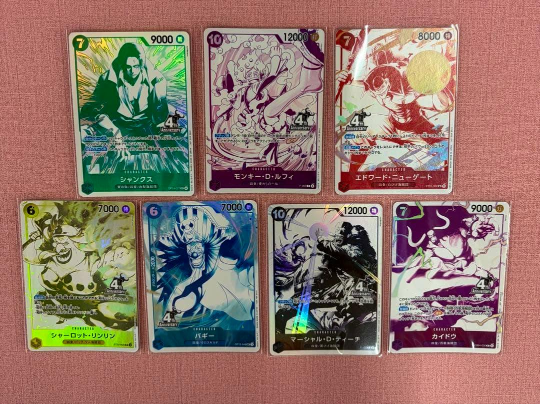 Eight ONE PIECE trading card fronts laid out on a pink surface showing various character artwork and "4th Anniversary" promo markings.