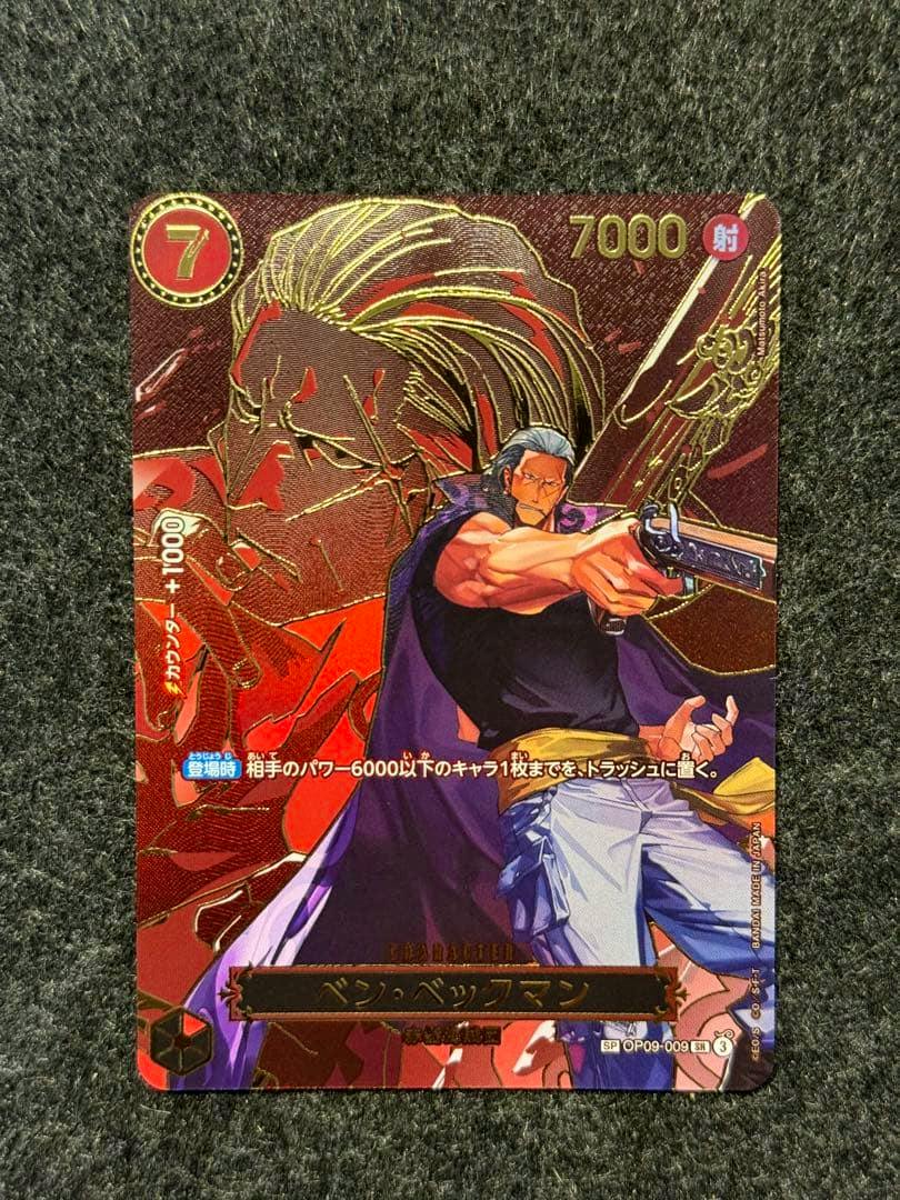 Photo of the front of the One Piece trading card (Ben Beckman SR) showing the character art, printed Japanese text and numbers on a dark textured background.