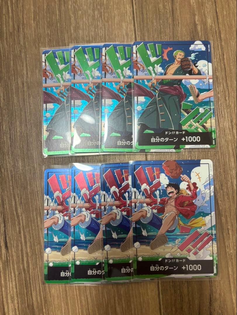 Eight One Piece trading cards (four Luffy and four Zoro Don cards) arranged on a wooden surface.