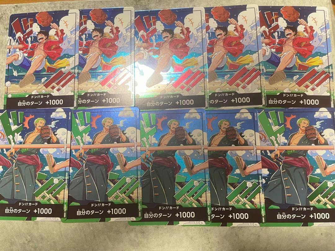 Photo of multiple ワンピースカード ドン!!カード trading cards laid flat showing character artwork and the '自分のターン +1000' text.