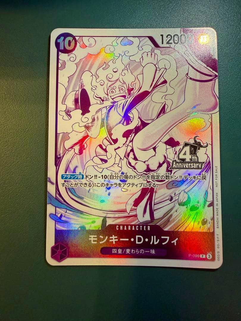 Front of the One Piece trading card (モンキー・D・ルフィ P-099) showing holographic artwork of Monkey D. Luffy and Japanese card text.