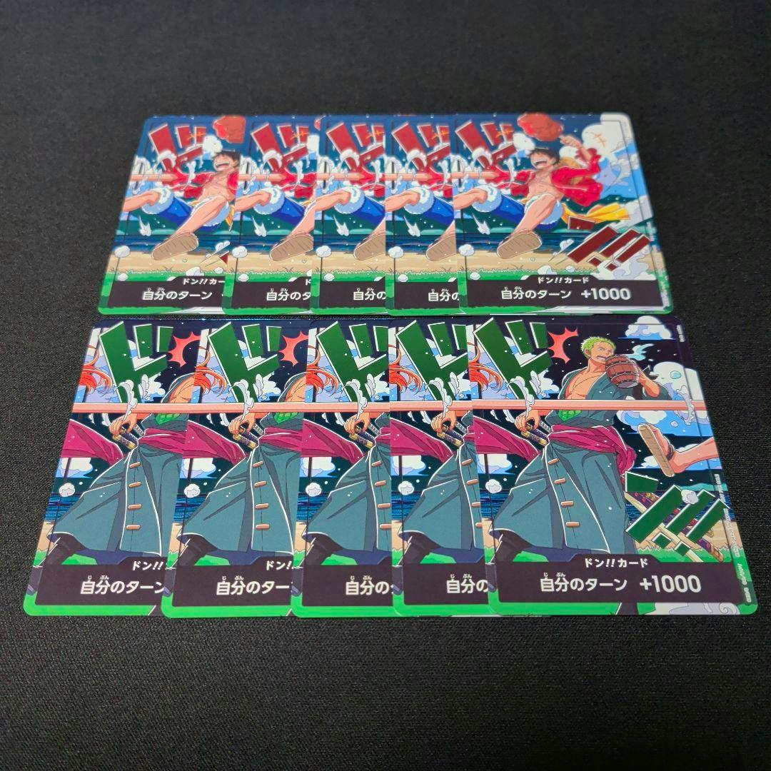 Photo of multiple One Piece trading card promo cards (Luffy and Zoro Don cards) arranged on a black surface.