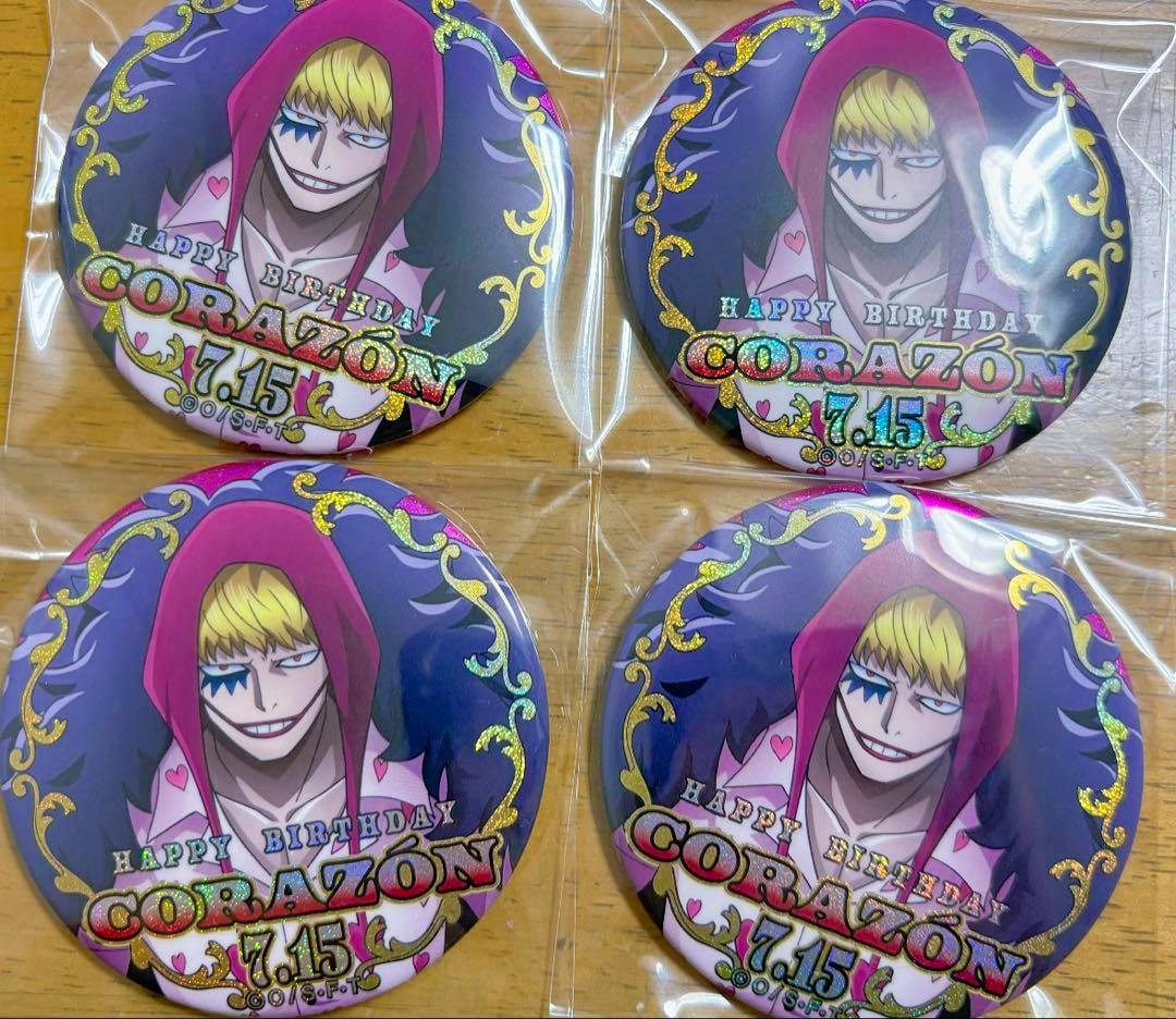 Four round ONE PIECE Corazon can badges showing the character illustration and “HAPPY BIRTHDAY CORAZON 7.15” text, arranged in a 2x2 grid in plastic sleeves on a wooden surface.