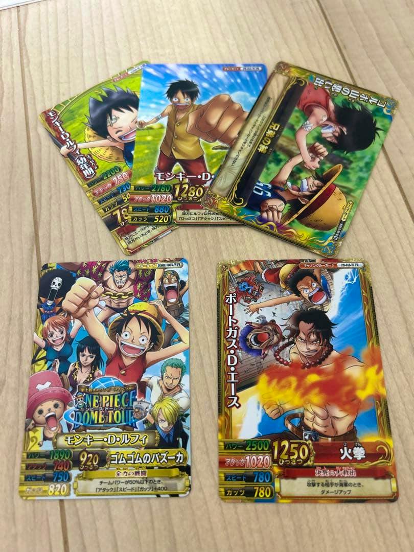 Several One Piece trading cards, including Monkey D. Luffy and Portgas D. Ace, arranged on a wooden surface.