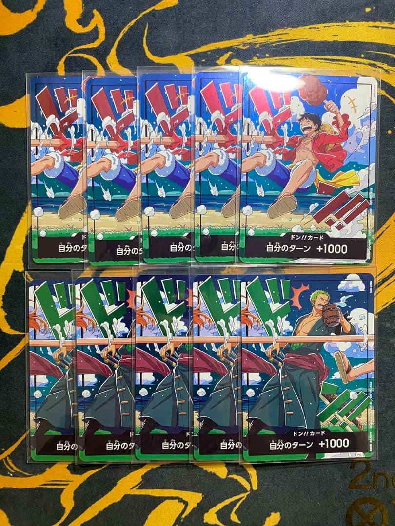 Photo of ten One Piece trading cards arranged in two rows, five cards with a jumping character on the top row and five cards with a standing character on the bottom on a patterned surface.