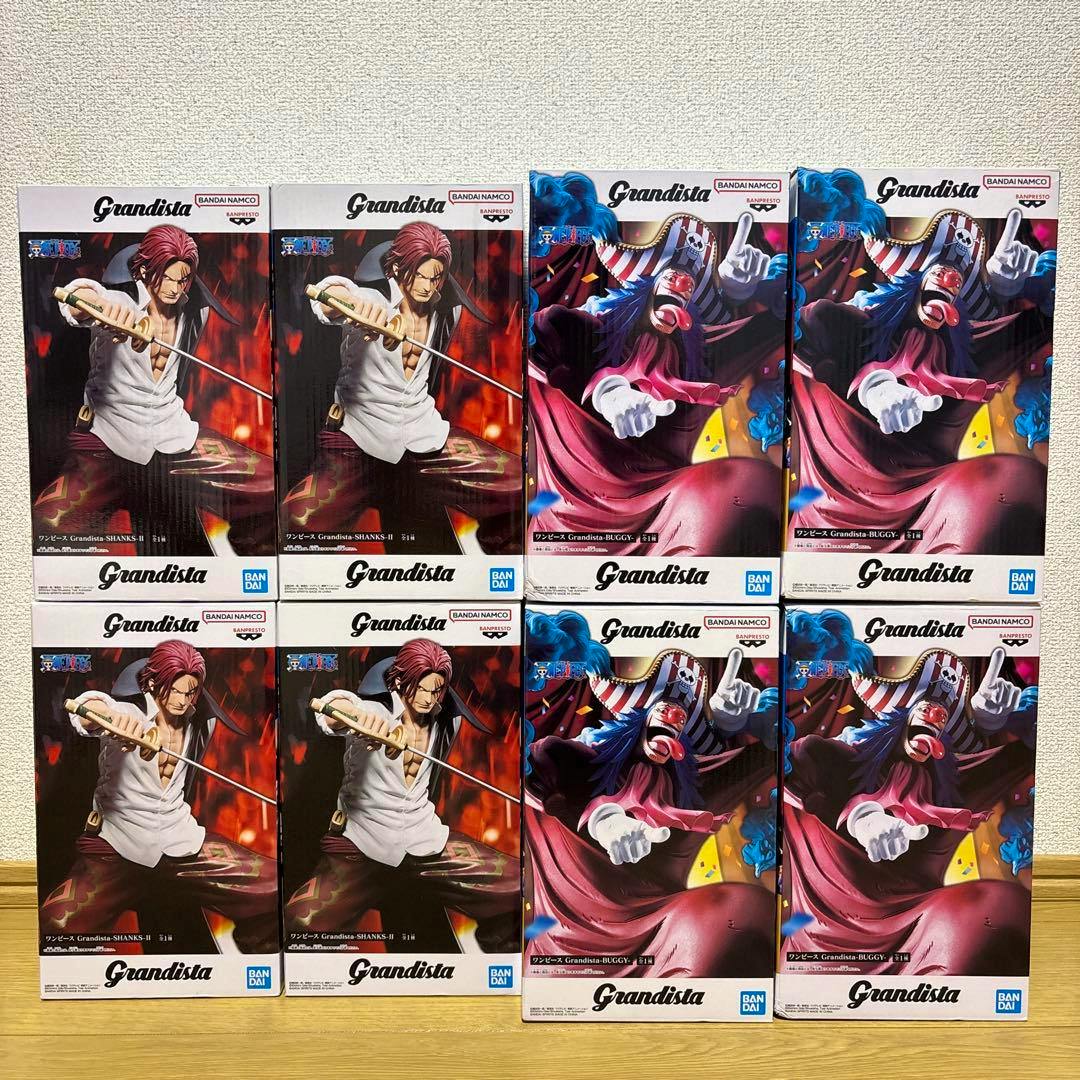 Eight Grandista One Piece figure boxes (Shanks and Buggy) arranged in a two-by-four grid on a wooden floor.