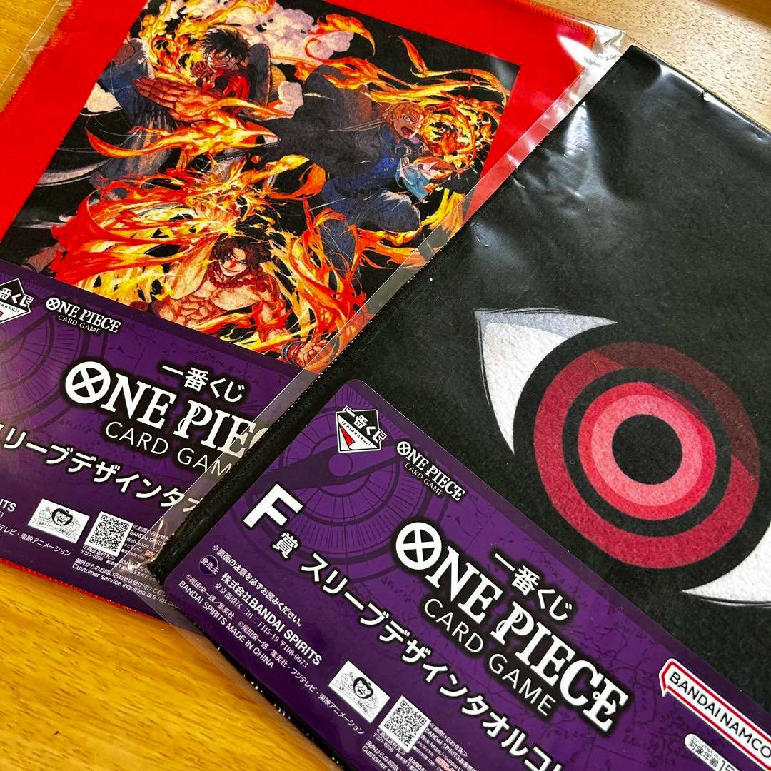 Two packaged One Piece F‑prize sleeve-design towels (handkerchiefs) showing Imu-sama art and an eye motif on a wooden surface.