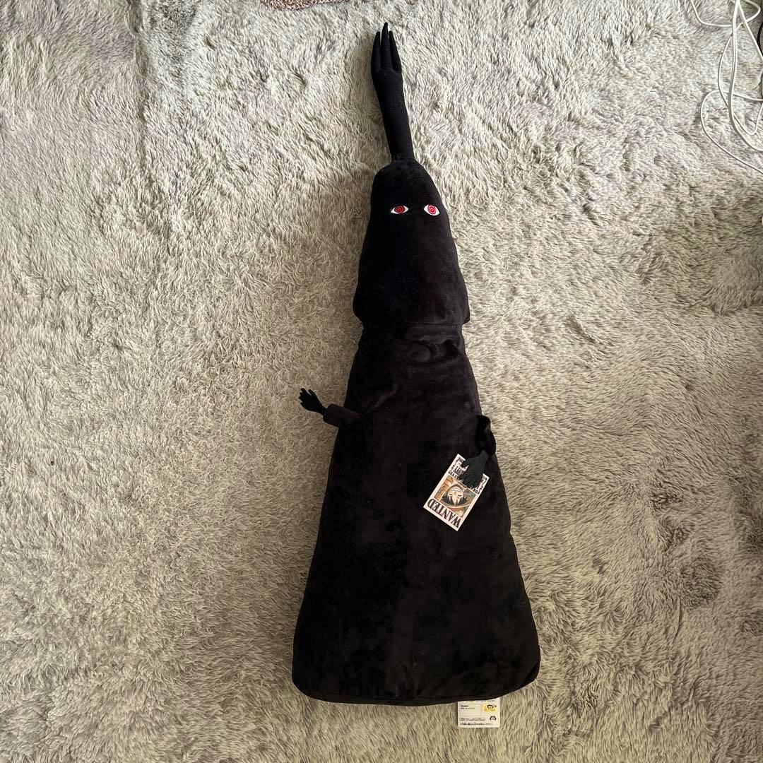 A black IMU-sama plush toy from One Piece laid flat on a grey carpet with its tag visible.