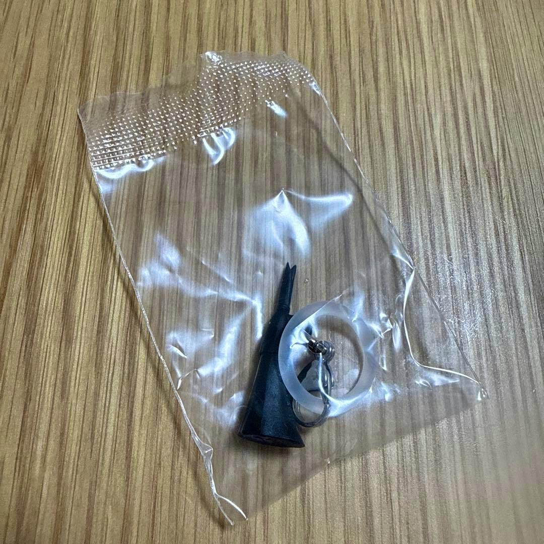 A small black plastic keychain charm and a clear ring are shown inside a sealed clear plastic bag on a wooden surface.