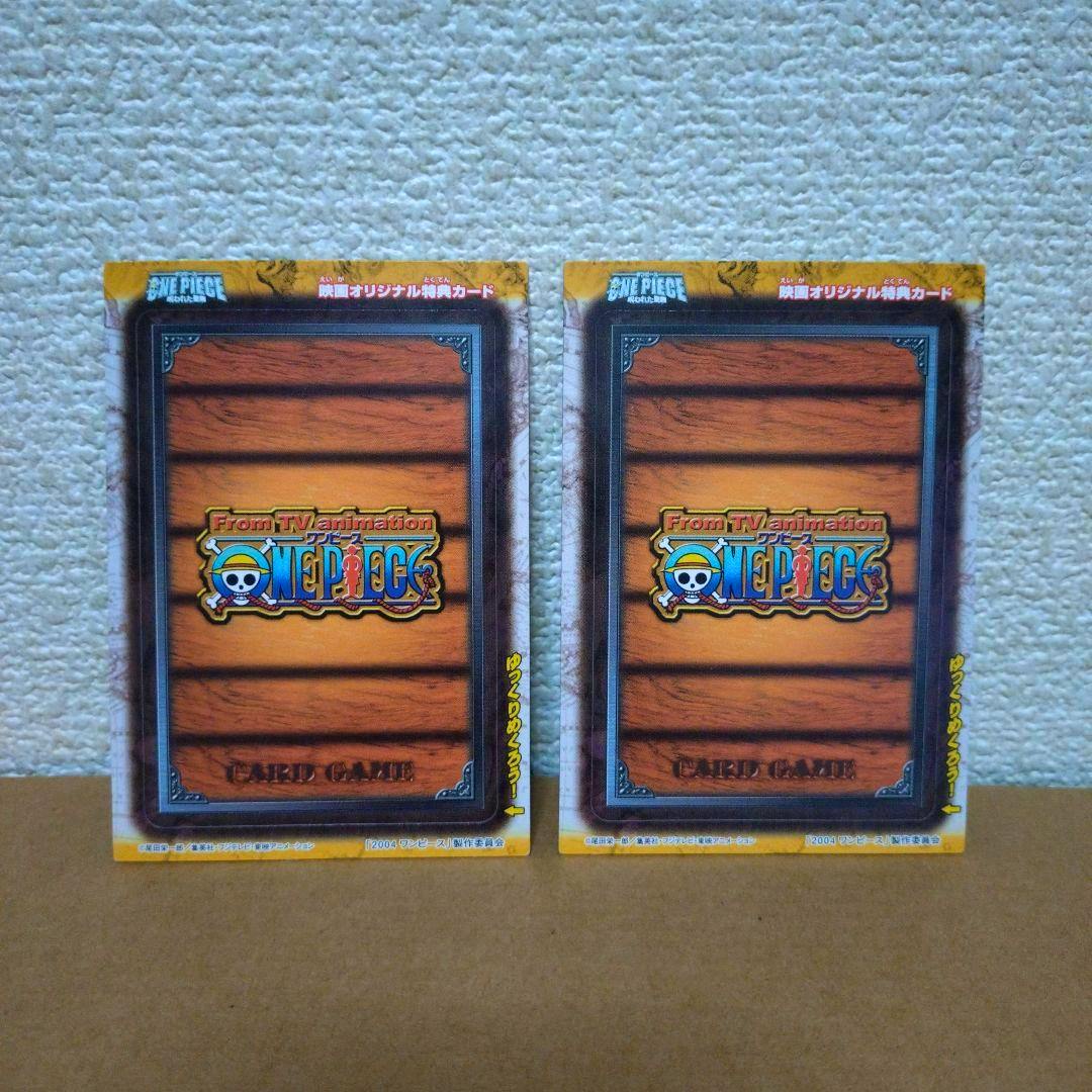 Two One Piece trading cards shown with their wood-patterned card backs visible against a textured wall.