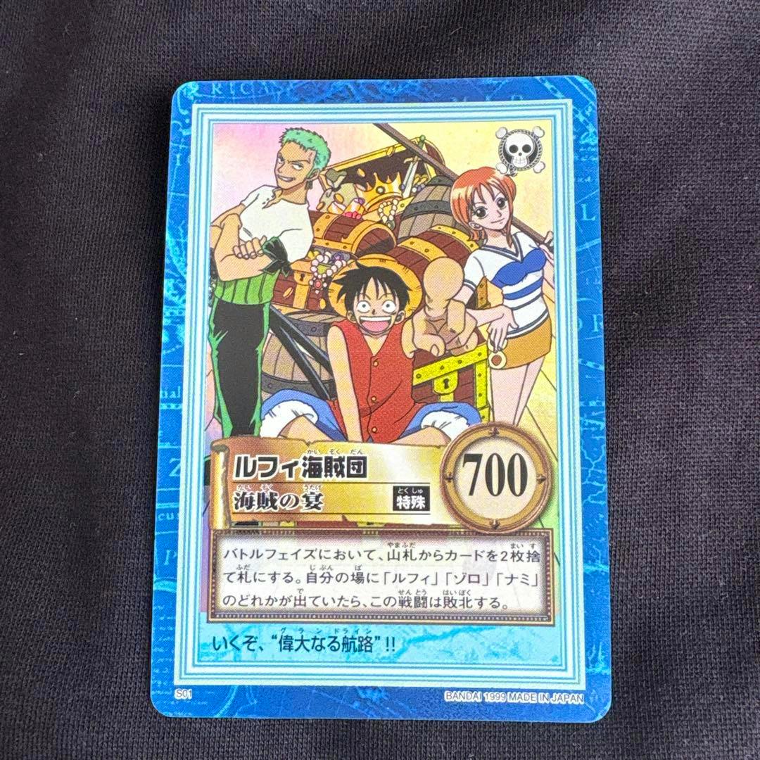 Front of a One Piece trading card showing Luffy, Zoro, and Nami with a blue border and a 700 value, placed on dark fabric.