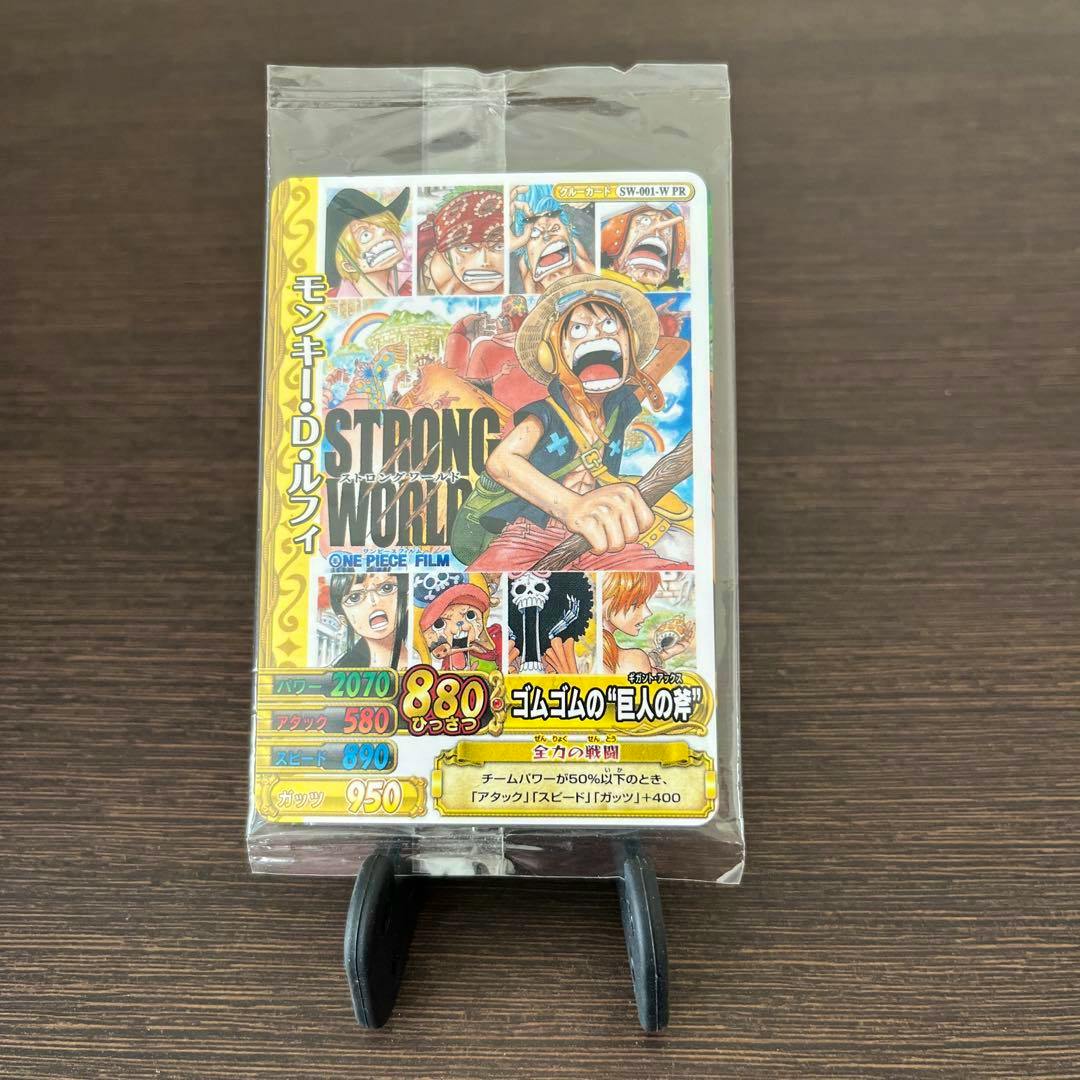 Sealed One Piece STRONG WORLD bonus card showing Luffy artwork in clear plastic packaging on a dark wood surface.