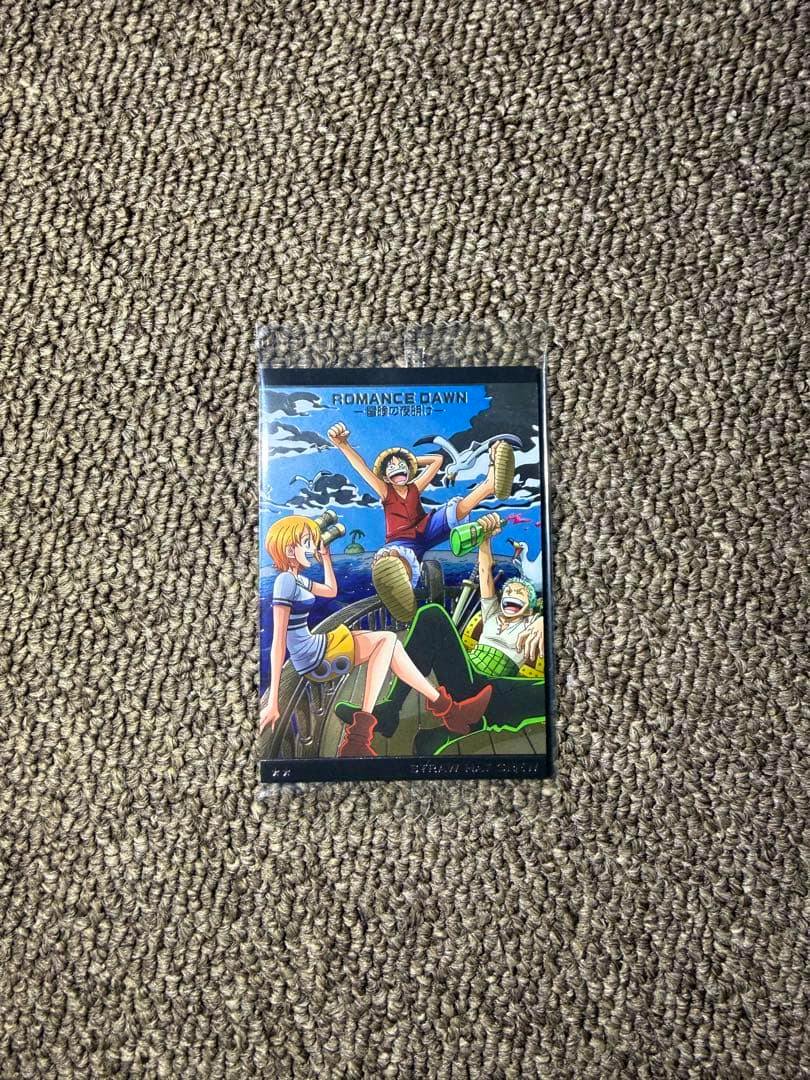 A plastic One Piece card sleeve (ROMANCE DAWN) showing Straw Hat crew artwork on a carpet background.