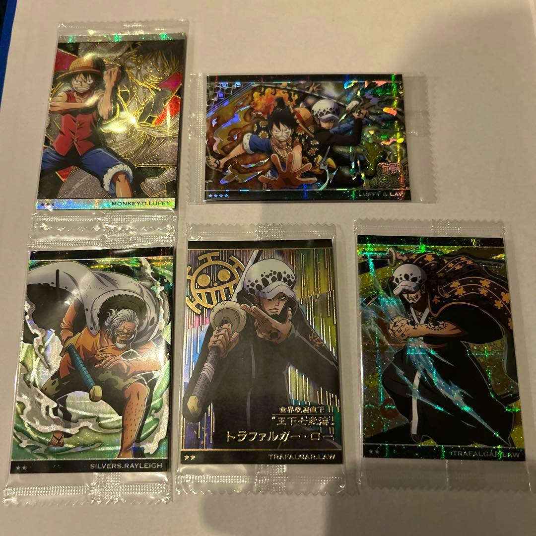 Six holographic One Piece wafer photocard cards in individual plastic sleeves laid out on white paper.