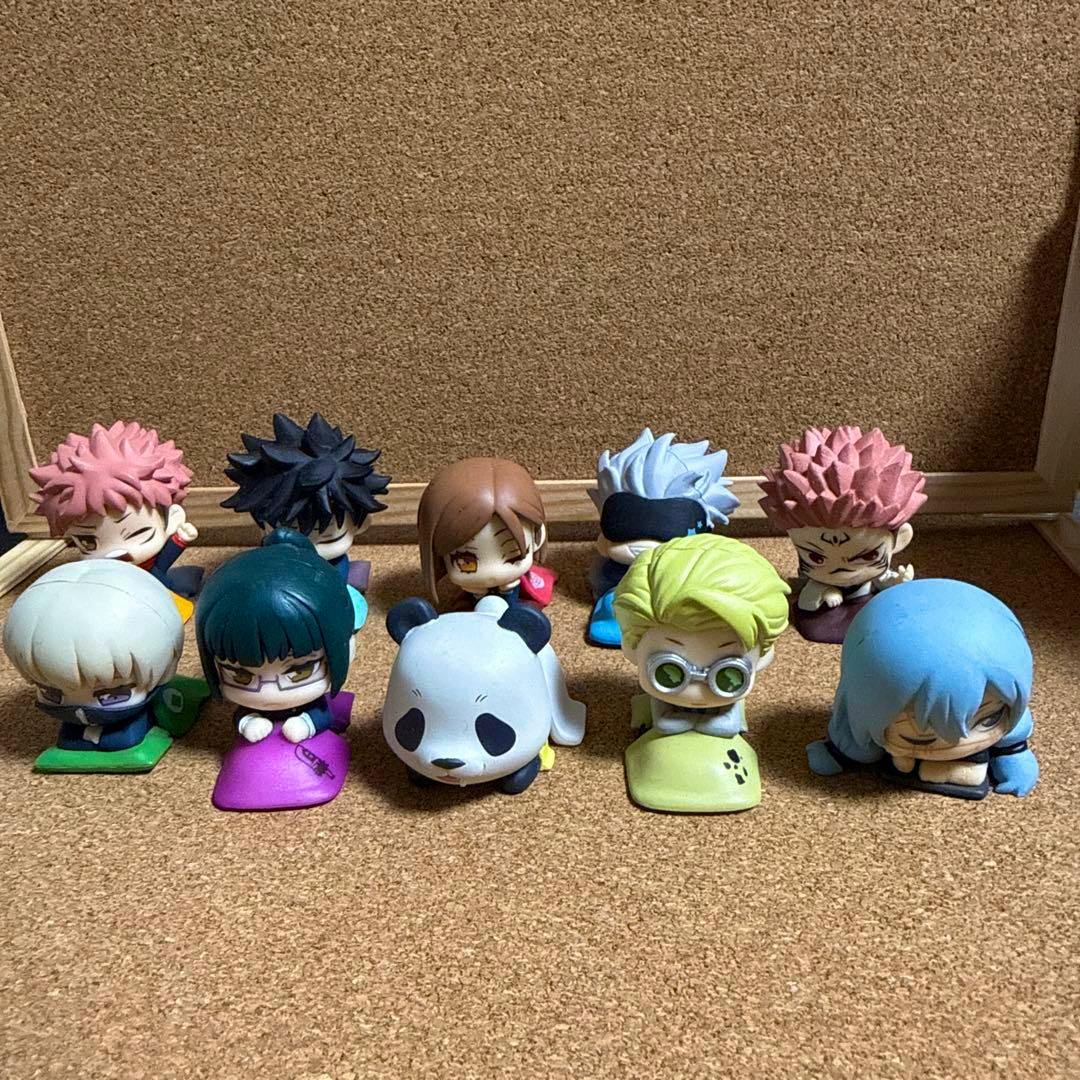 Ten small chibi plastic figures from Jujutsu Kaisen arranged on a corkboard background.