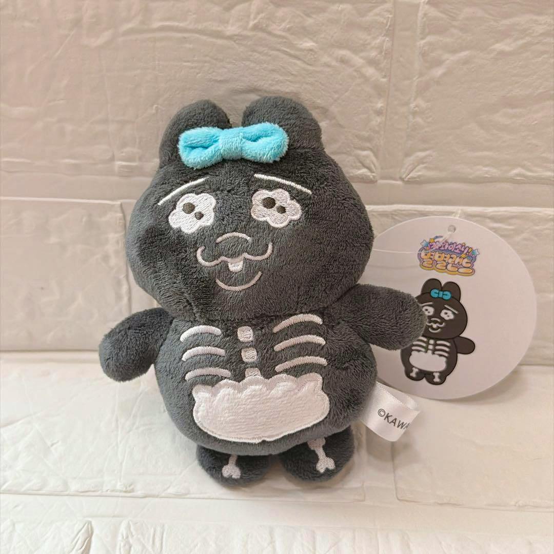 Front view of a gray rabbit plush keychain with white embroidered x-ray skeleton details and a small blue bow, shown with its round tag.