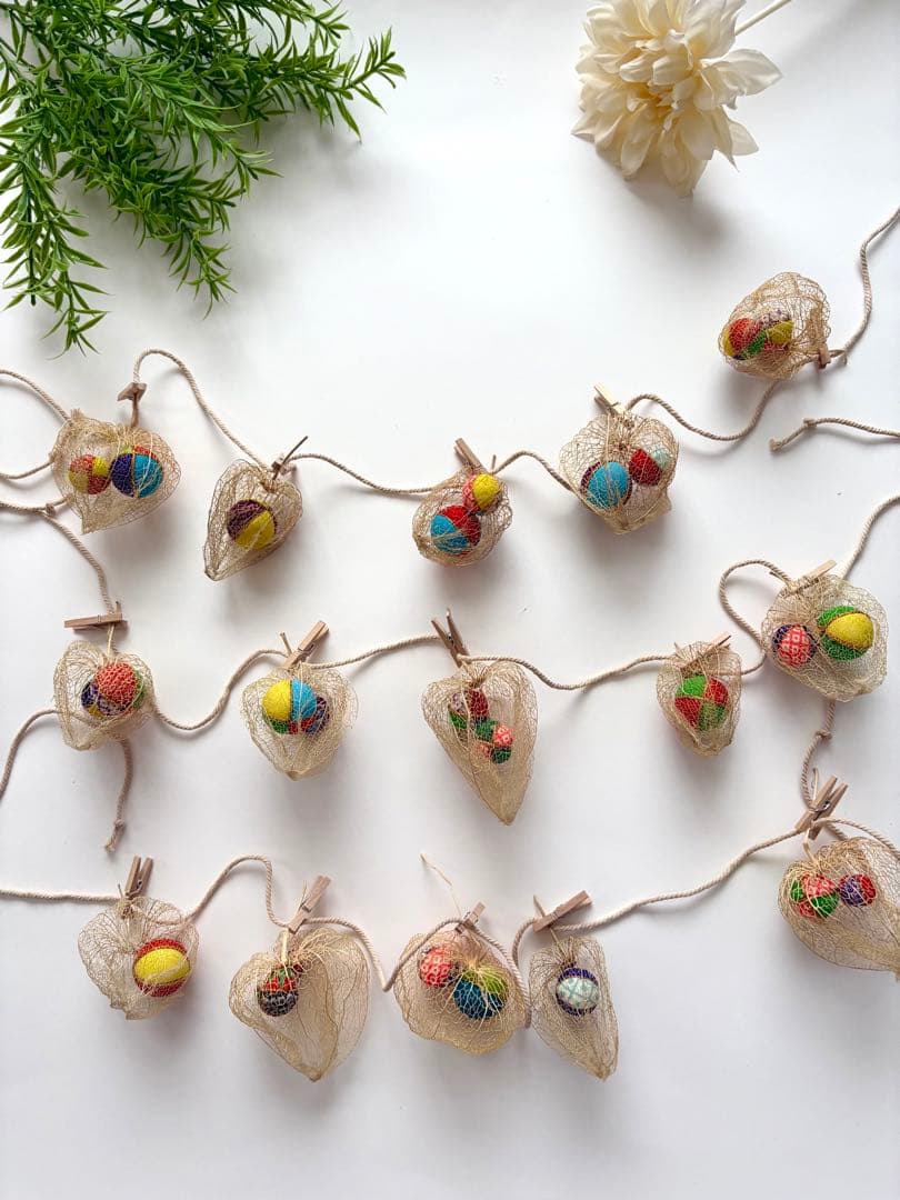 A fabric physalis-style garland with openwork lanterns each containing small colorful temari balls, laid out on a white background.