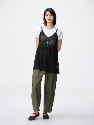 Model wearing the knit camisole tunic in black over a white T-shirt and green pants against a plain light background.