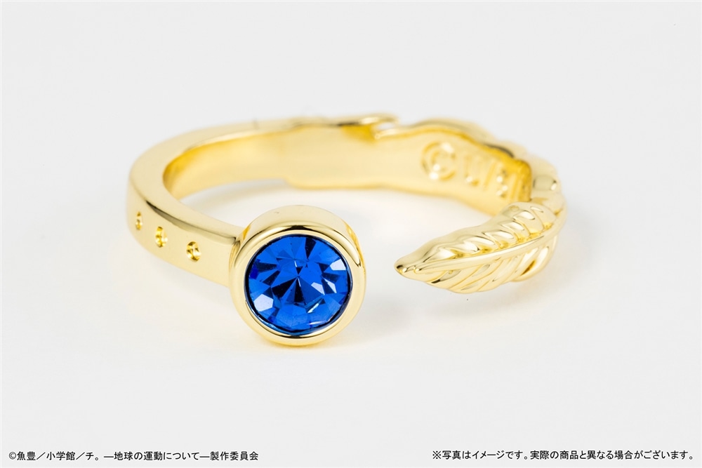 Photograph of the gold-colored non-precious metal ring with a single blue faceted stone and a feather-detail open band.