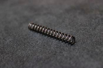 Close-up photo of a tappet spring for Next Generation AEGs lying on a dark surface.