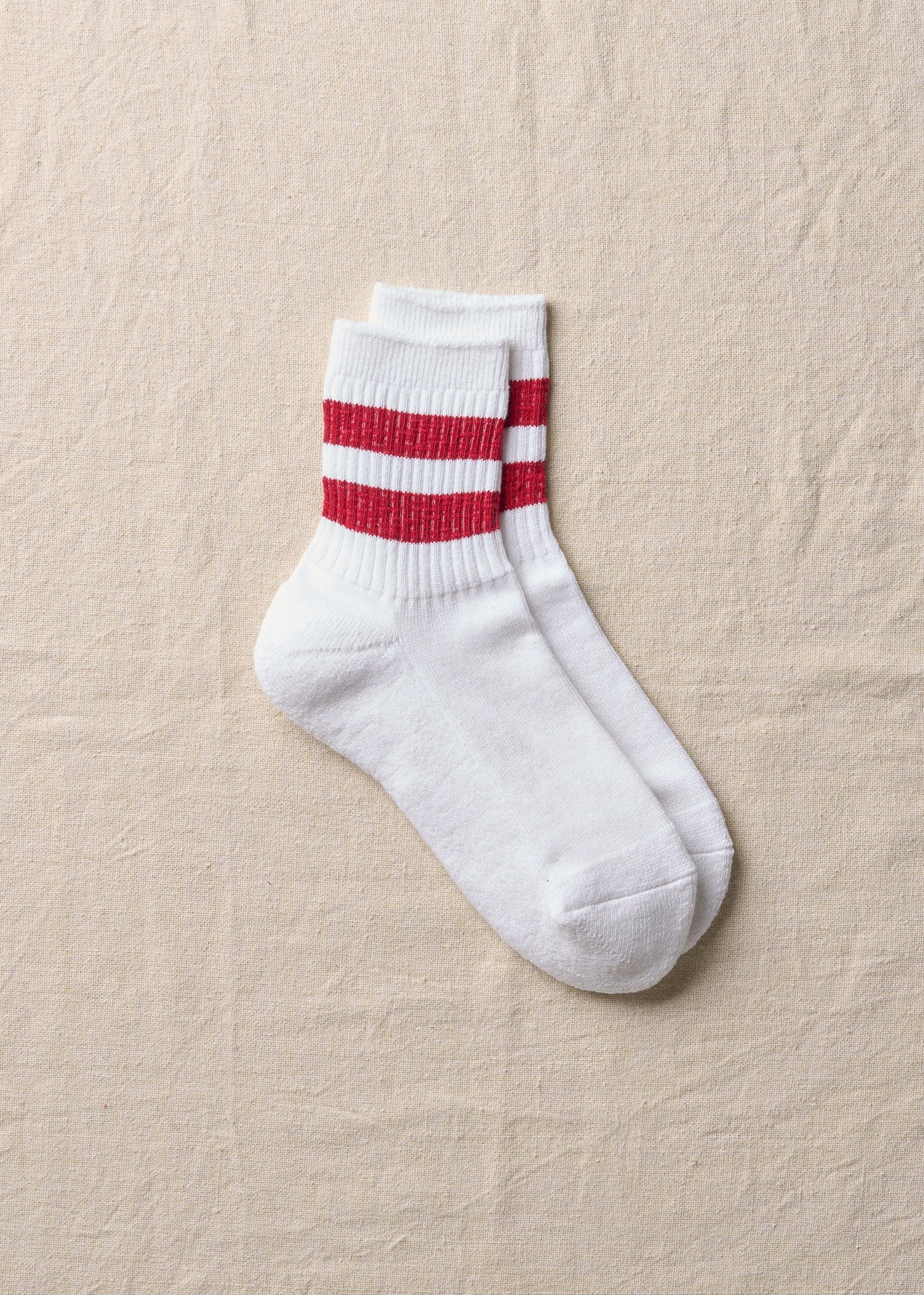 White men's crew socks with two red ankle stripes laid flat on a fabric surface.