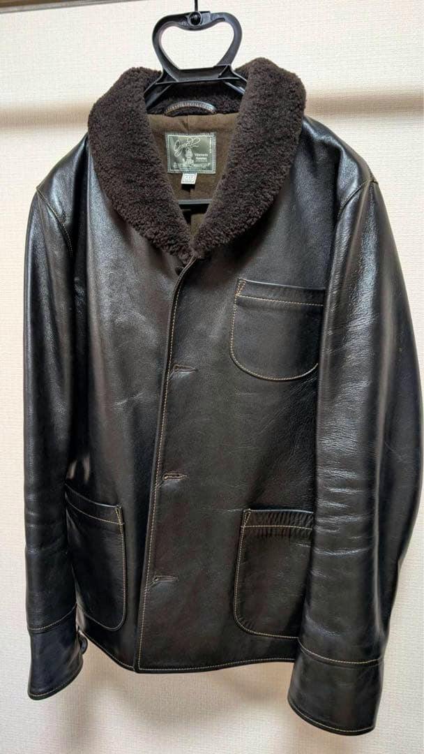 Front view of a men's black horse leather jacket with a dark brown boa collar hanging on a hanger.