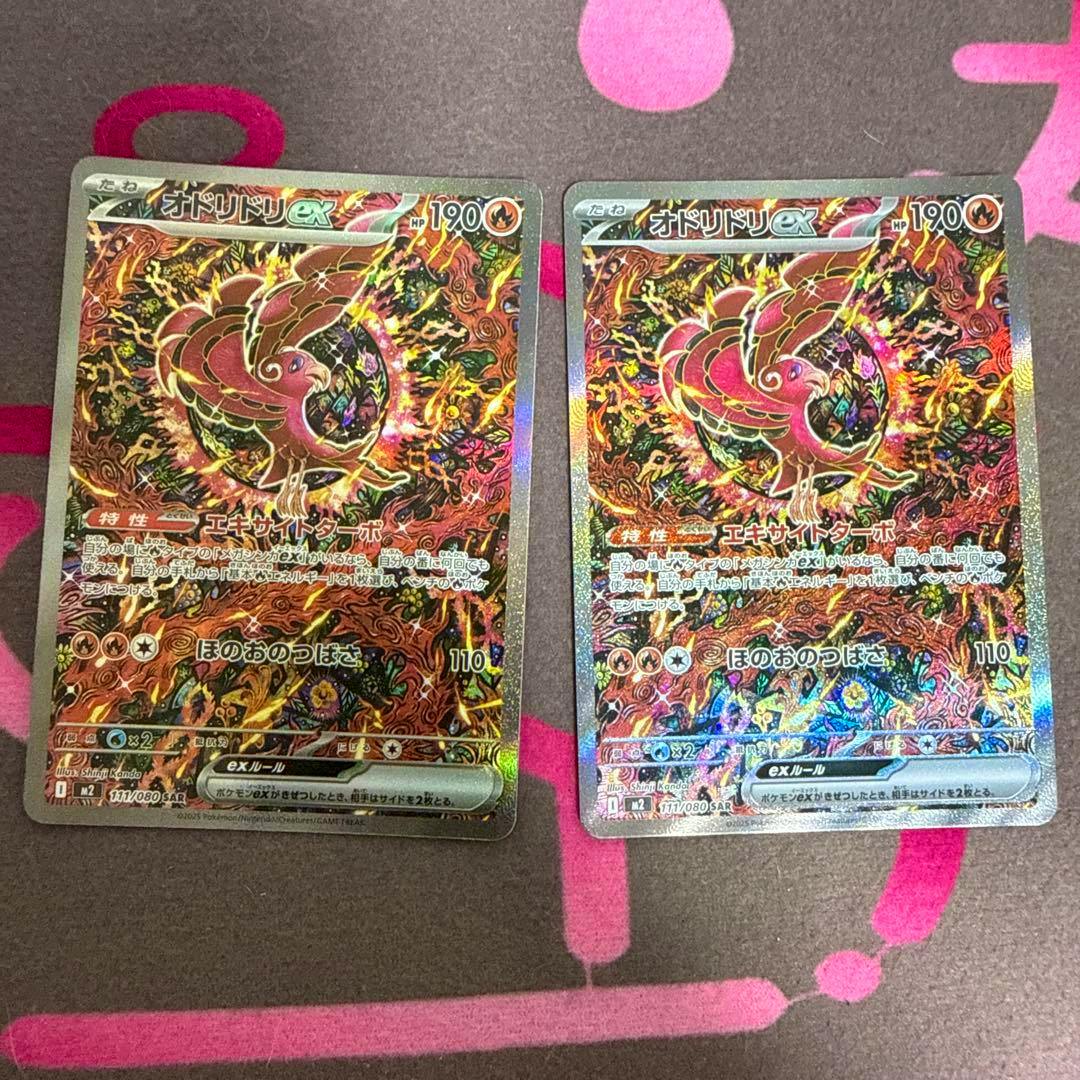 Two trading cards showing the holographic front artwork of オドリドリex SAR MEGA 拡張パック インフェルノX 111/0802枚 placed side by side on a patterned surface.