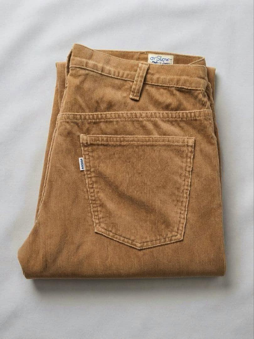 Folded beige corduroy pants showing the back pocket and waistband label.