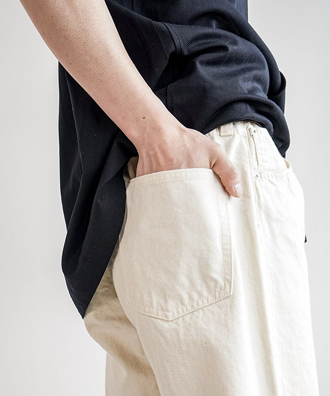 Close-up of a model wearing the kinari men's denim pants showing the rear pocket and hand.