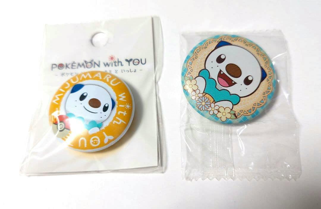Two packaged ミジュマル (Oshawott) can badges shown front-facing, one on a 'POKÉMON with YOU' backing card and one in clear plastic.