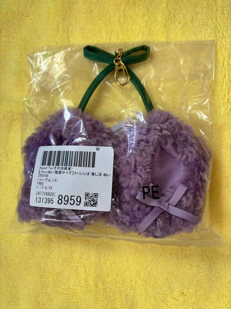 Purple fluffy mini poncho for plush toys with a green strap and gold clip, shown sealed in clear plastic packaging on a yellow background.