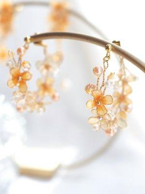 Close-up of two gold-colored floral dangle earrings with orange flower motifs and small beads on a display stand.