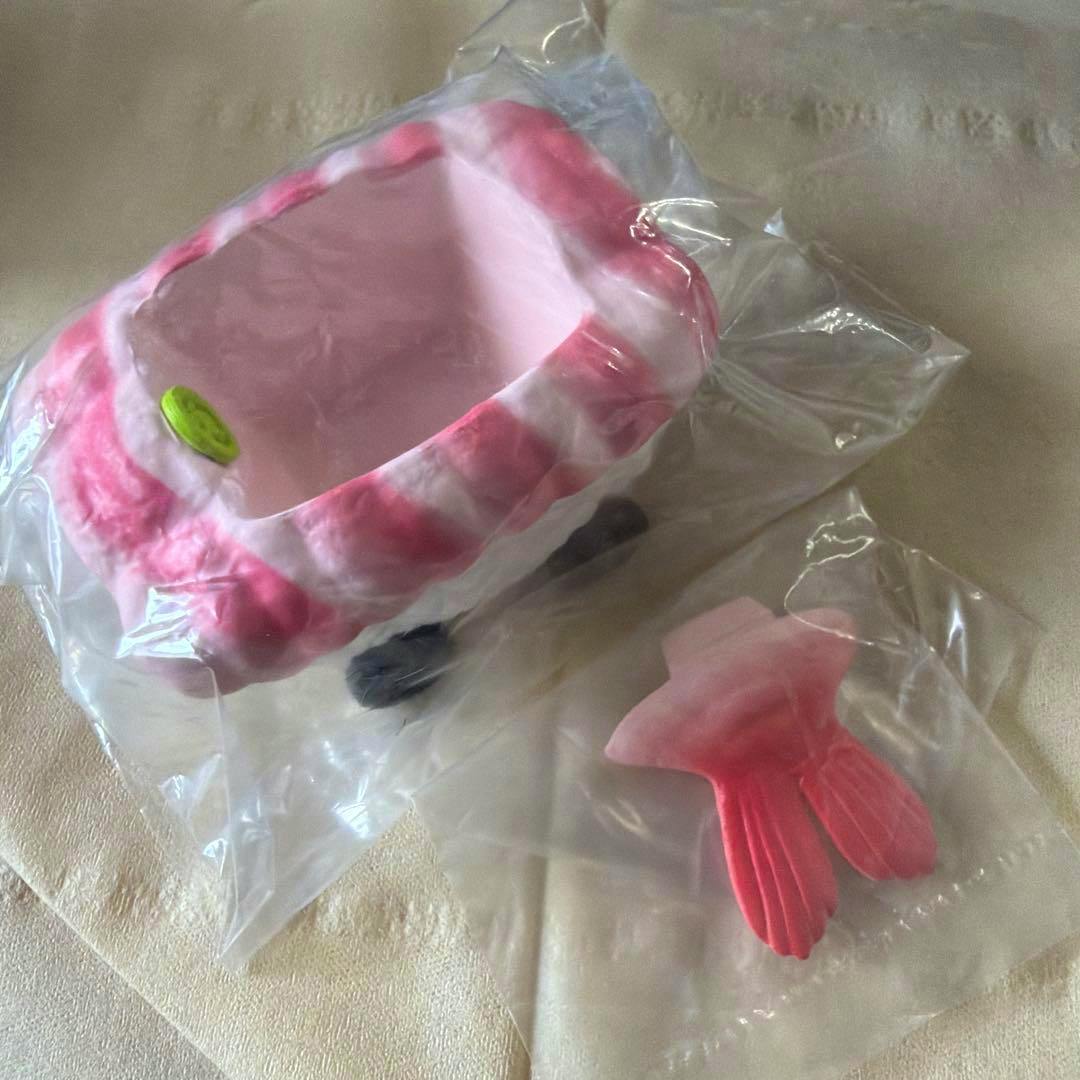 Photograph of the shrimp sushi car plastic figure partially packaged in clear plastic with the separate shrimp tail piece shown beside it.