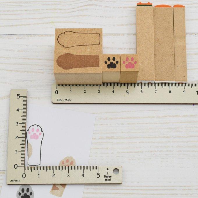 Wooden cat-paw stamps lined up by a ruler with sample paw-print impressions on paper.