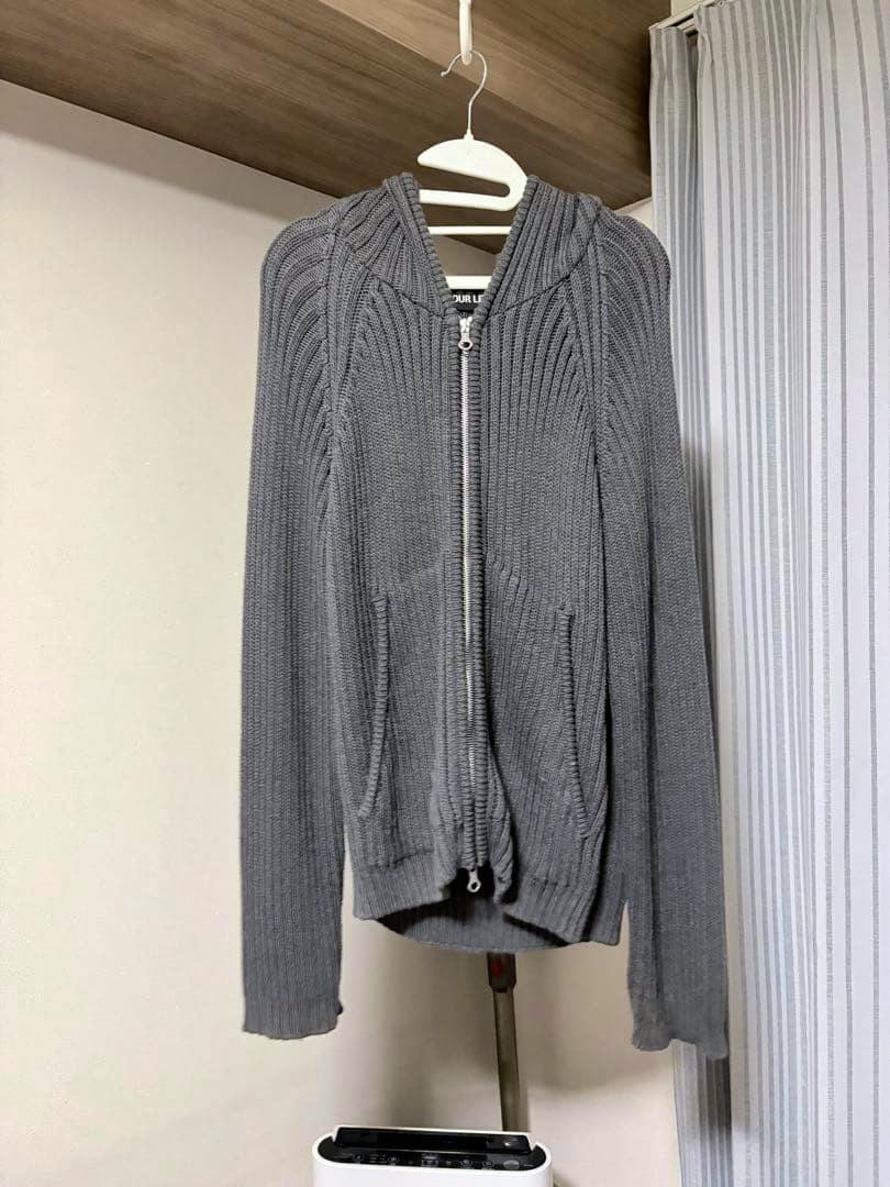 Gray OUR LEGACY zip-up knit hoodie sweater hanging on a hanger, front view showing zipper and front pockets.