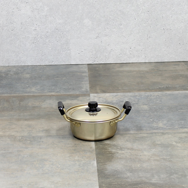 Stainless steel pot with lid and two black handles sitting on a tiled surface.