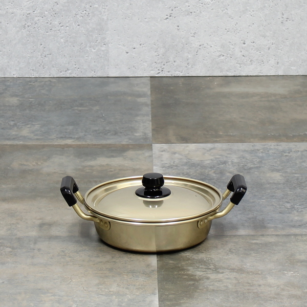 Shallow stainless steel pot with lid and black handles photographed on a tiled surface.