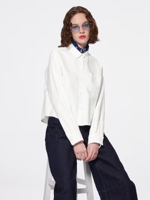 Female model seated on a stool wearing a white Oxford short shirt shown front view.