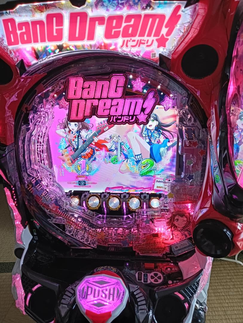 Close-up front view of a BanG Dream! pachinko machine lit in pink, showing the playfield and control panel.