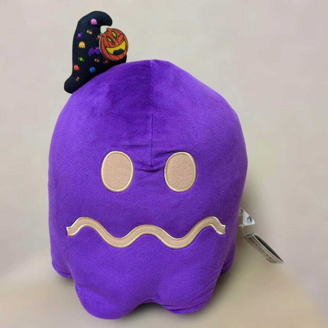 Front view of a purple Pac‑Man ghost plush showing embroidered eyes, a wavy mouth, and a Halloween-themed tag.