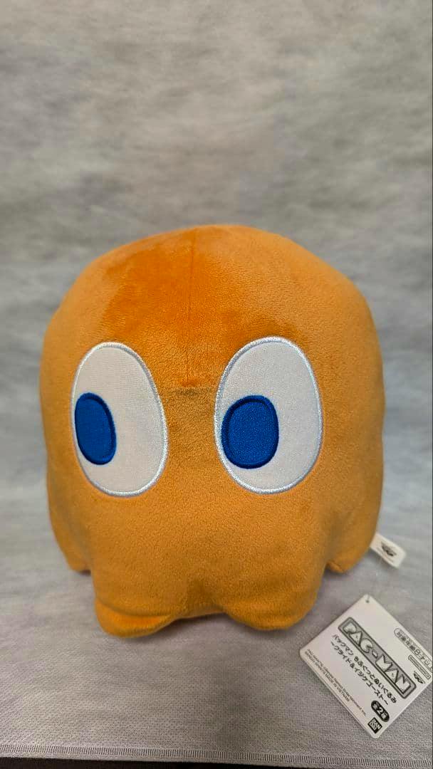 Front view of an orange Pac‑Man ghost plush with blue-and-white embroidered eyes and a tag visible at the lower right.